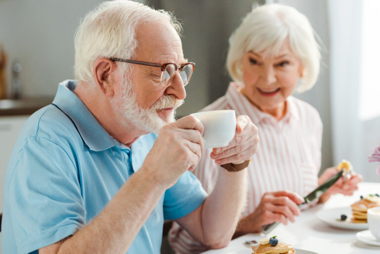 Selective focus of senior man drinking coffee by smiling wife wi